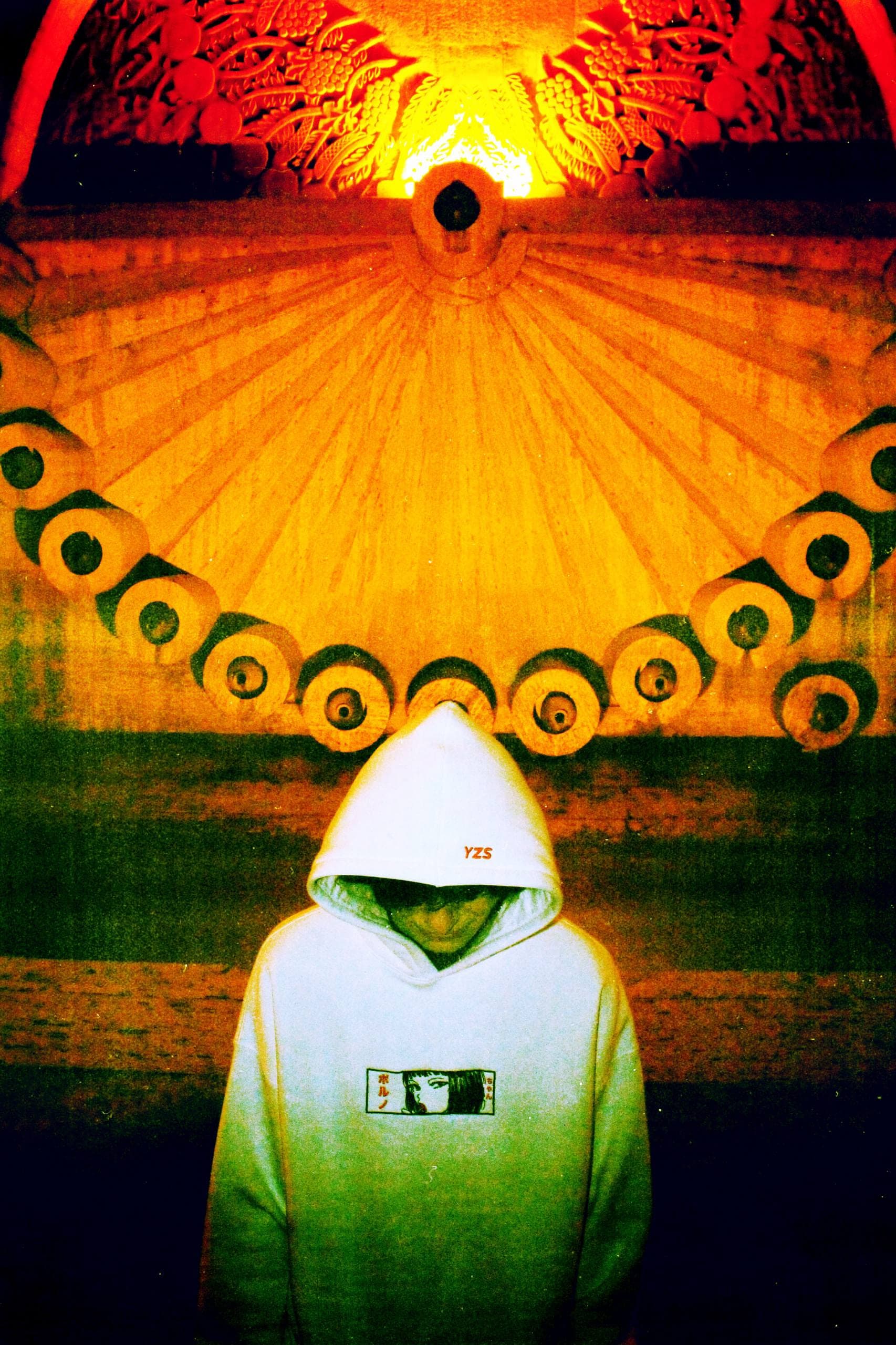 A figure in a white YZS hoodie standing beneath a carved stone sun