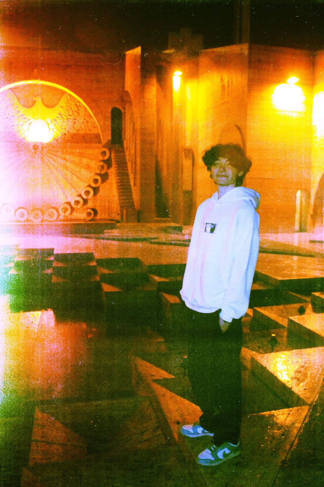 A figure in a white YZS hoodie in a concrete plaza at night